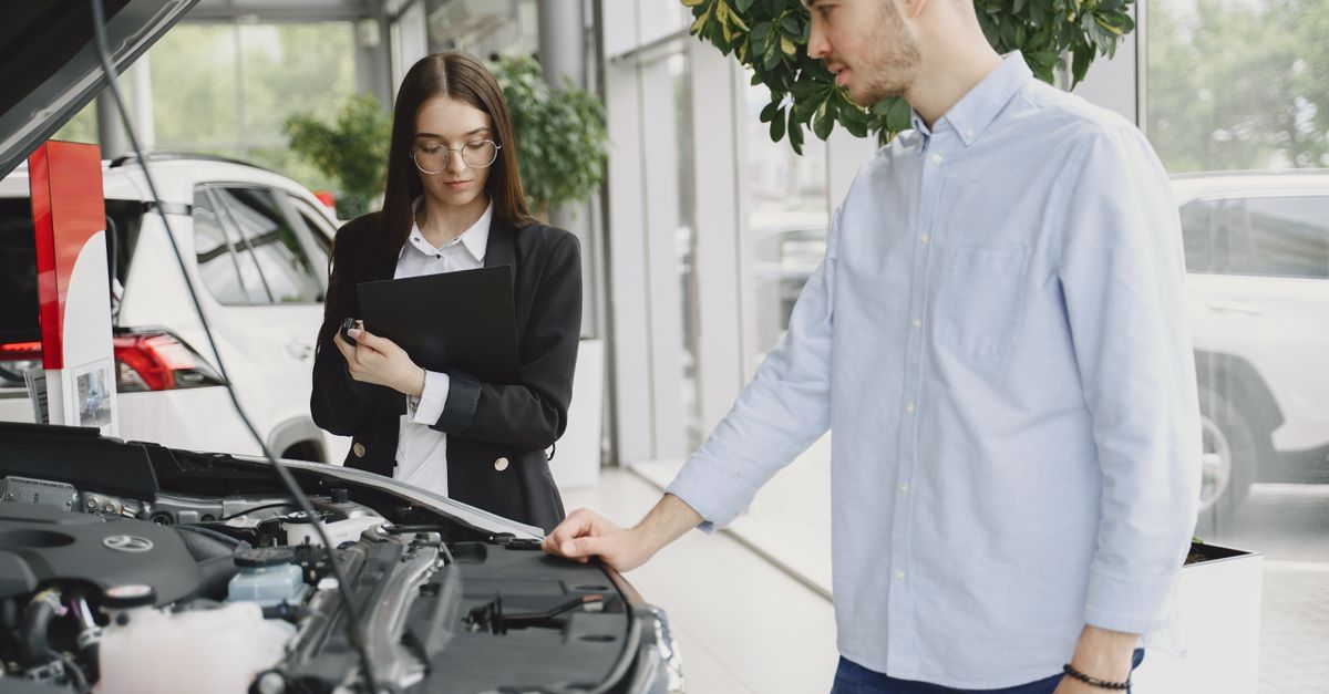 Man and woman examining car engine in dealership service area, focused on vehicle maintenance and functionality.