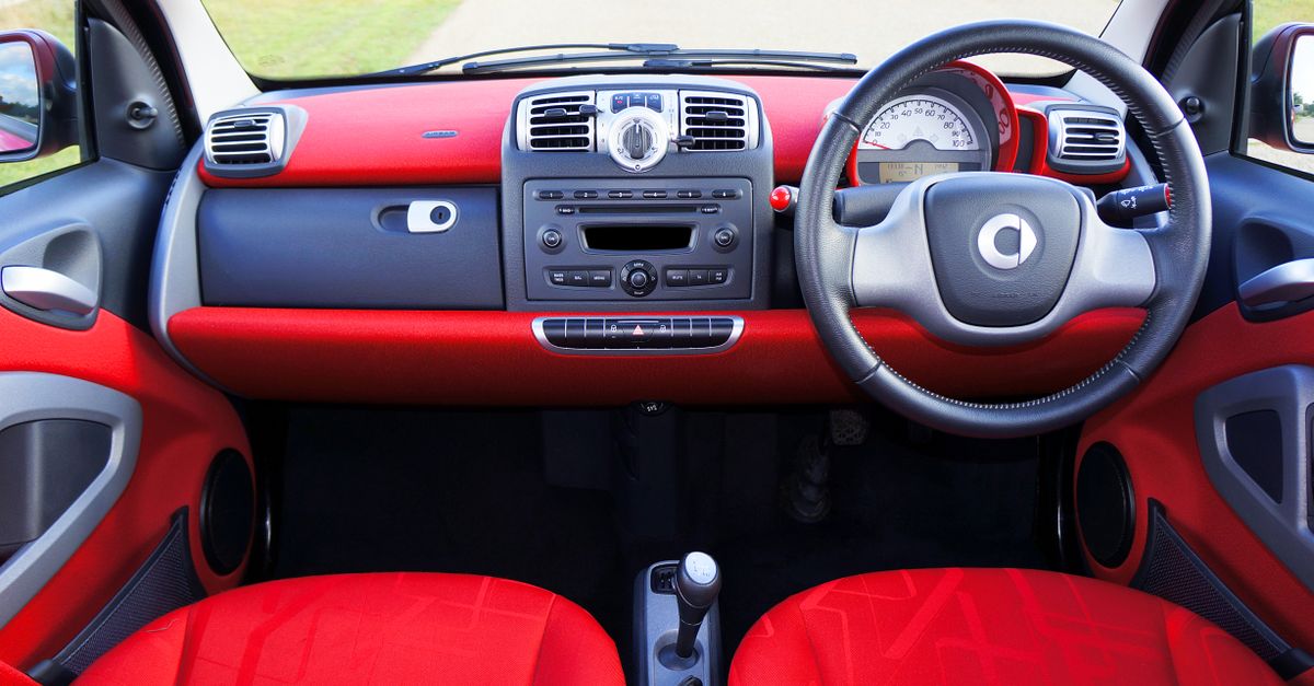 View of a compact car's red interior with a detailed dashboard and steering wheel.
