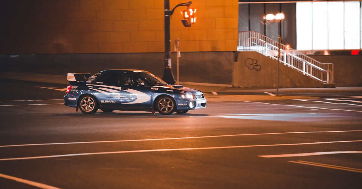 Rally car speeding through city streets at night, showcasing dynamic motion and urban setting.
