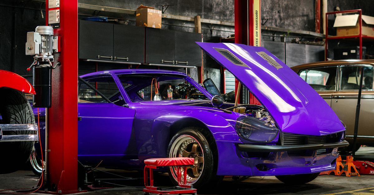 A classic car with a vibrant purple color in a mechanical workshop with its hood open.