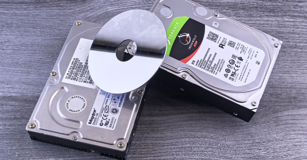Two computer hard drives and a shiny disk displayed on a wooden surface.