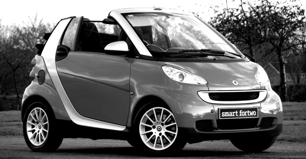 A stylish black and white image of a classic Smart Fortwo convertible parked outdoors.