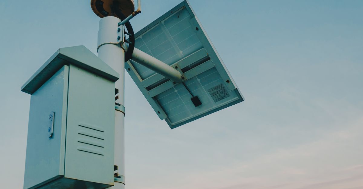 A solar panel paired with a security camera against a clear sky, representing renewable technology.