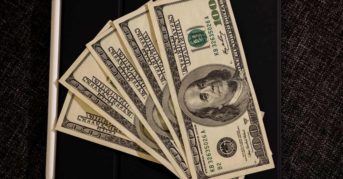 Spread of US dollar bills on black surface with stylus, symbolizing finance and technology.