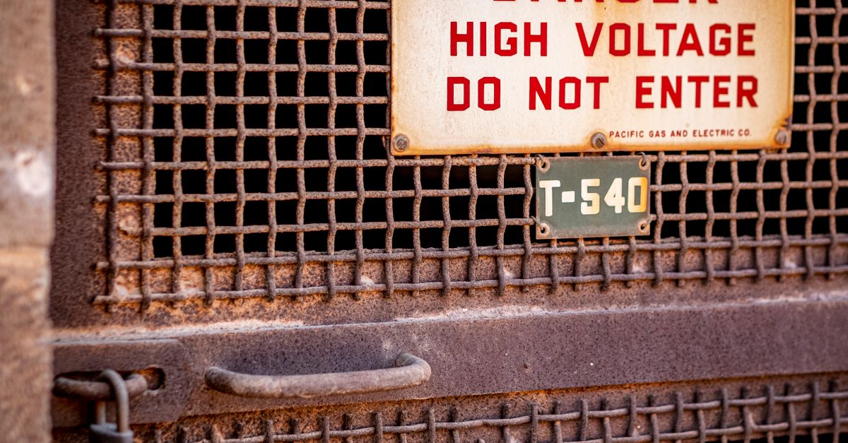 Close-up of a rusty industrial gate with a high voltage warning sign, conveying danger.