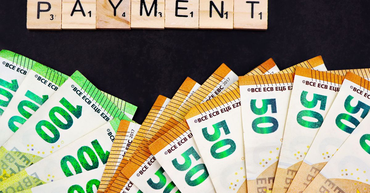 Euro banknotes fanned out with 'PAYMENT' spelled in Scrabble tiles, representing finance and commerce.