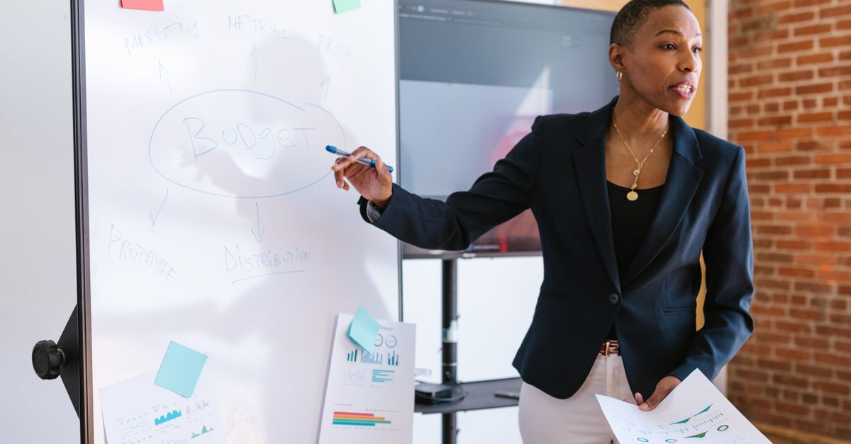 Professional businesswoman explaining budget strategy on a whiteboard during a meeting.
