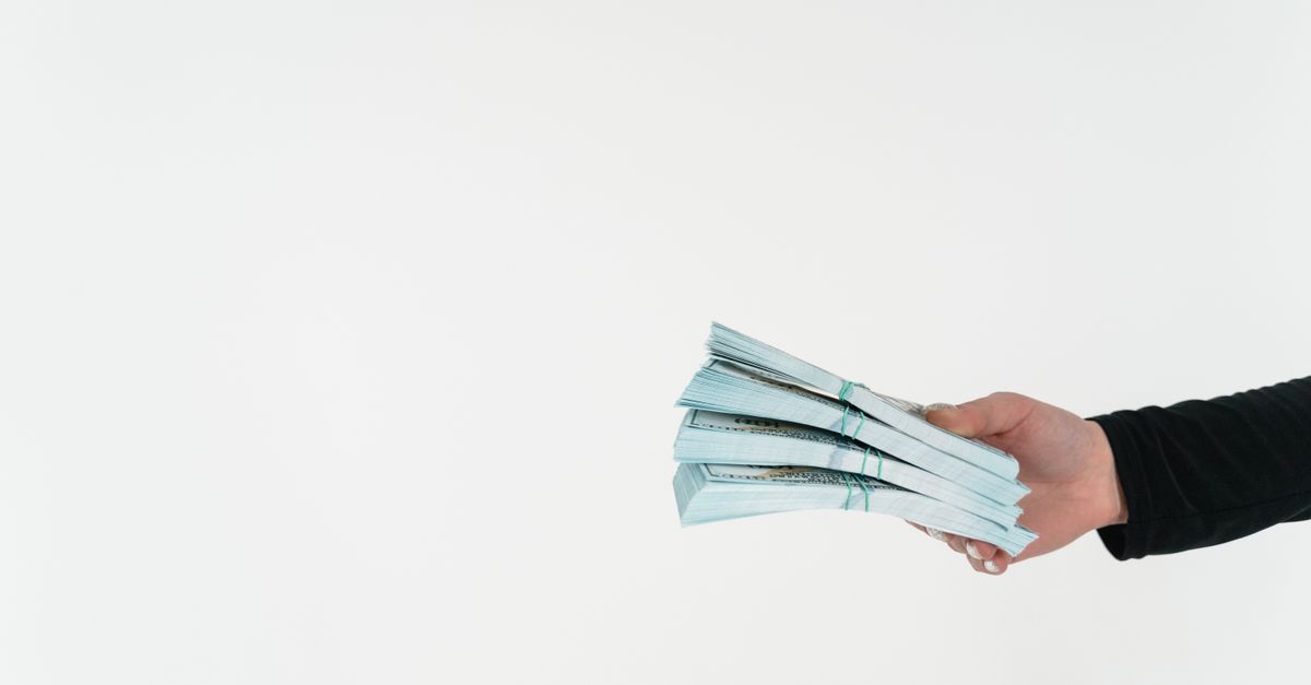 Close-up of a hand holding bundles of American dollar bills against a white background.