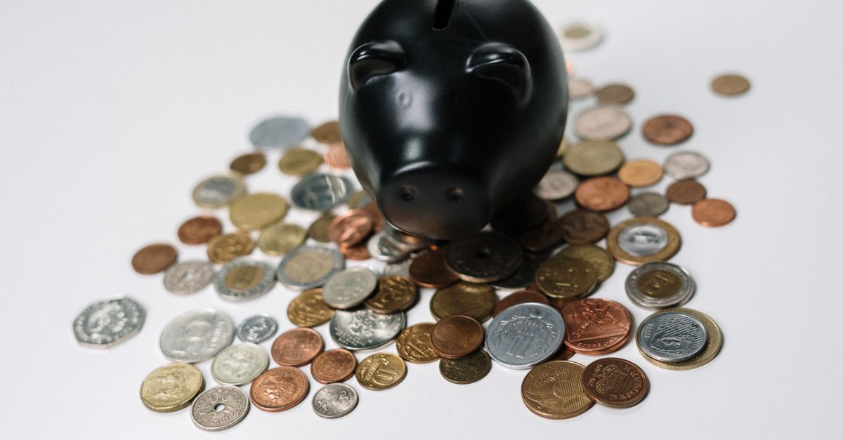 Black piggy bank surrounded by a variety of coins on a white surface, symbolizing savings and finance.