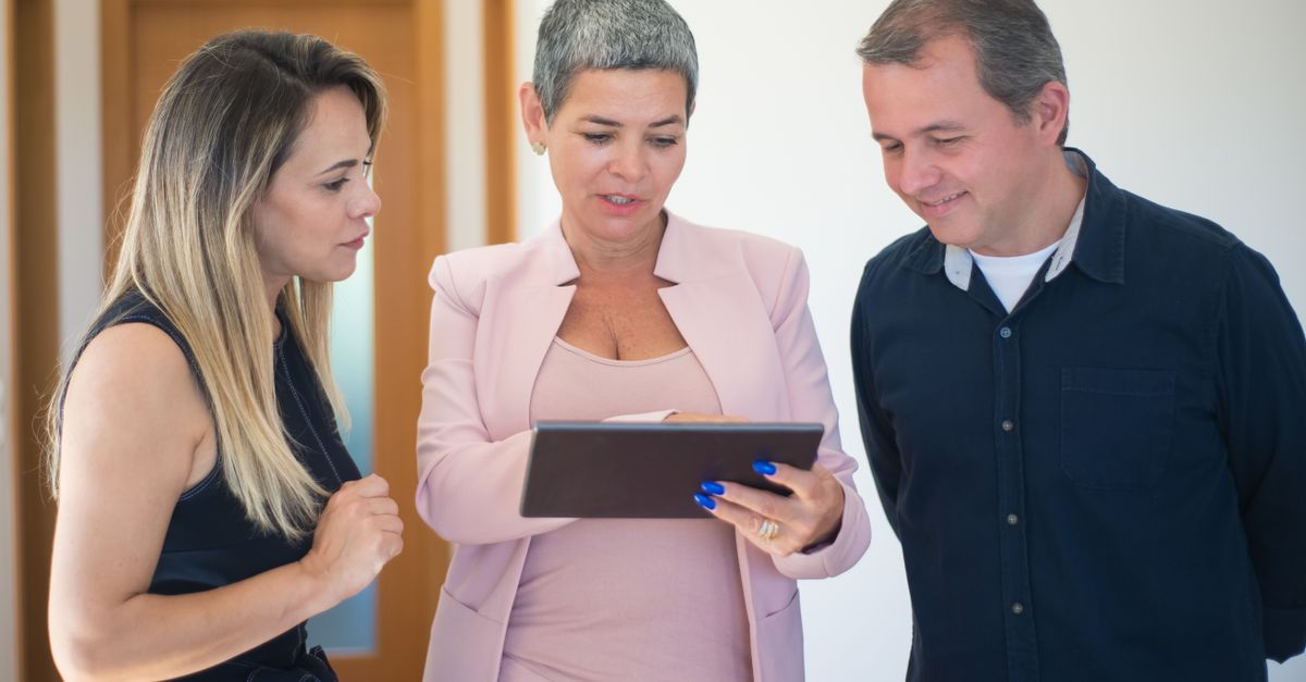 Real estate agent presenting property details to a couple using a tablet indoors.