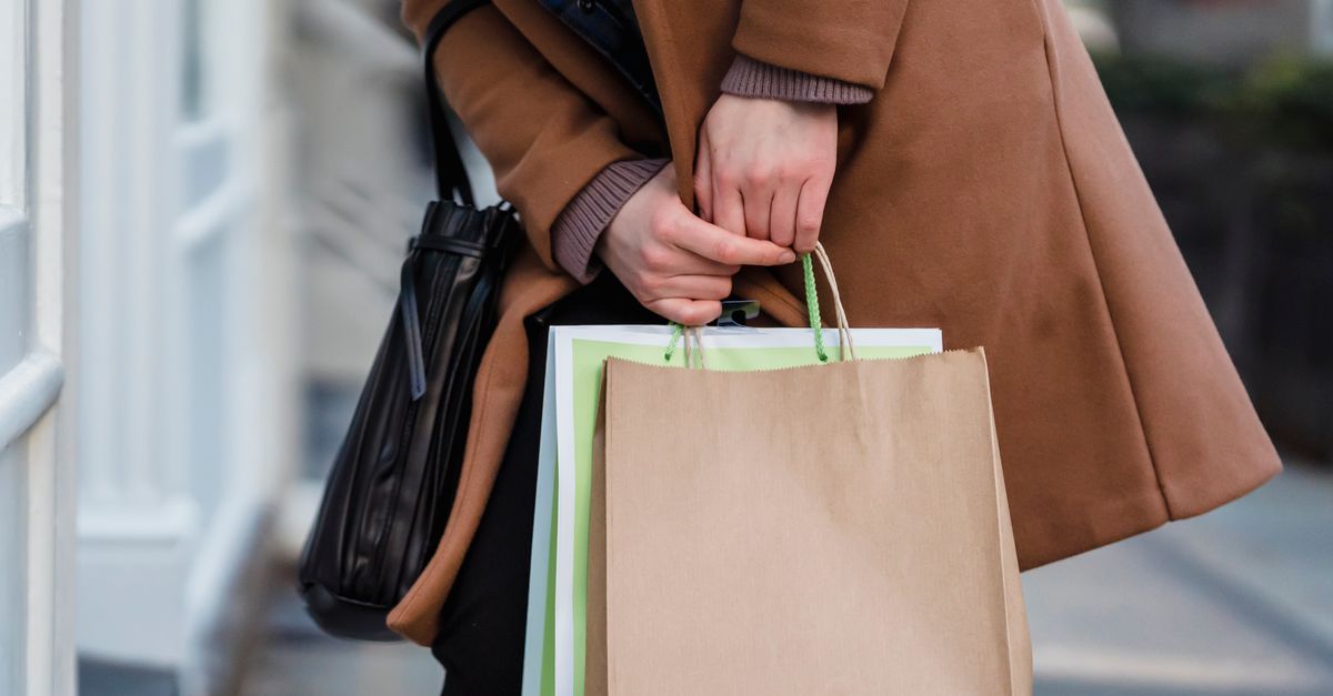 Crop unrecognizable female customer wearing coat standing with paper packets and handbag while shopping in city