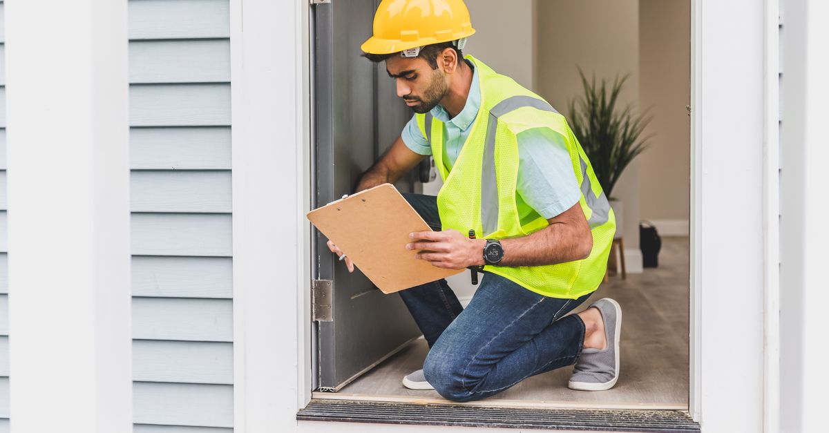 A home inspector wearing safety gear examines a house interior for safety compliance.