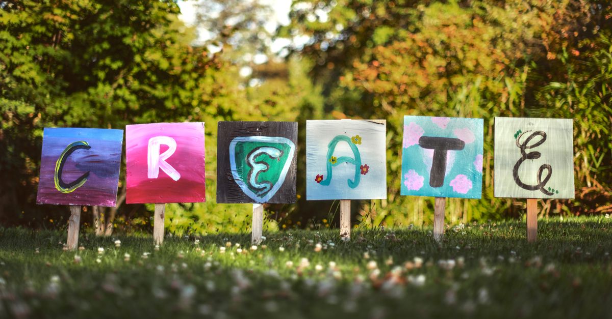 Vibrant painted signs spelling 'CREATE' in a lush outdoor garden setting.