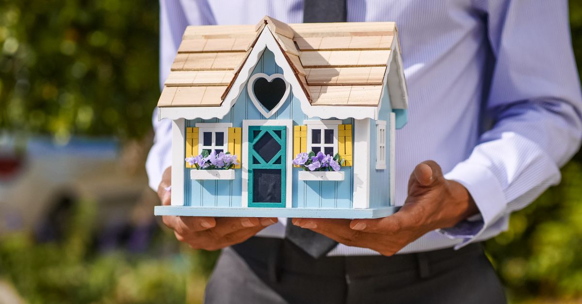 A businessman holds a detailed, colorful miniature house model. Ideal for concepts of real estate and property investment.