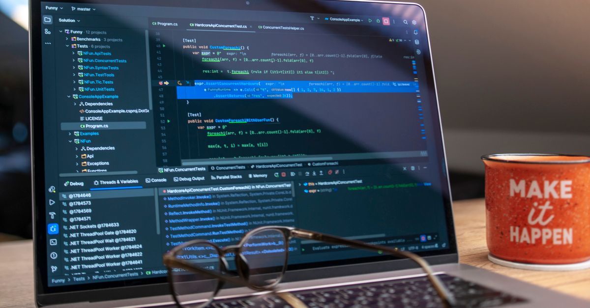 A laptop displaying code editor with a motivational mug that reads 'Make It Happen' on a workspace.