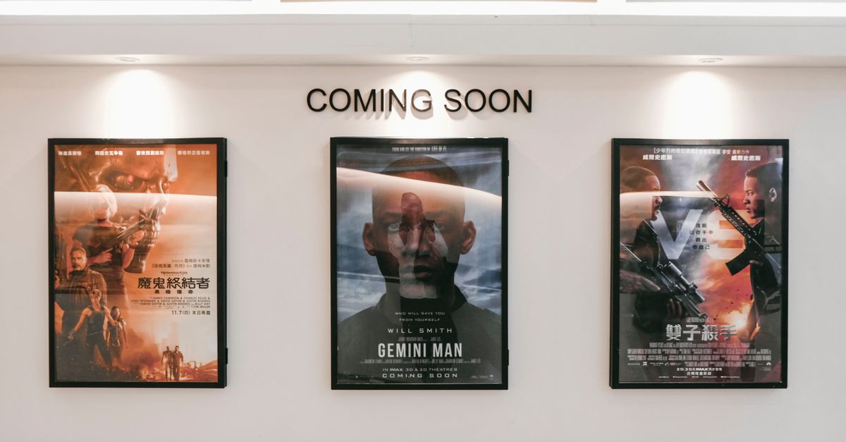 Framed posters of upcoming movies in a cinema hallway under 'Coming Soon' sign.