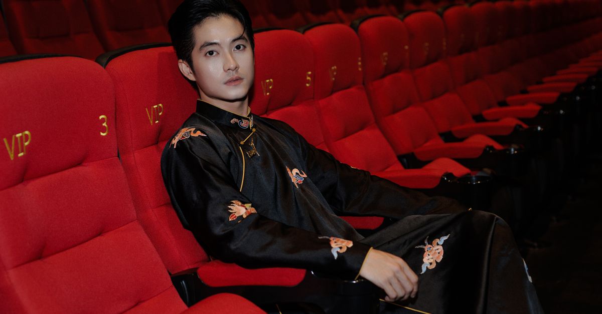 Man in traditional attire seated in VIP cinema with vibrant red seats.