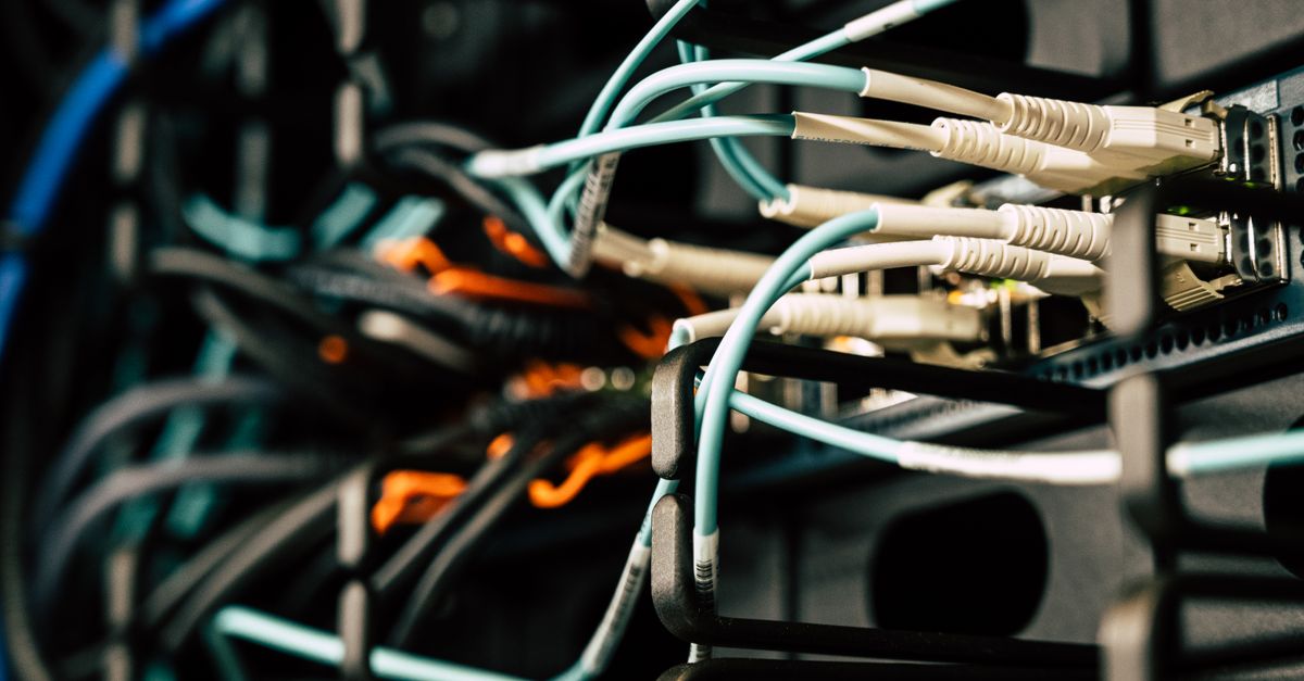 Various tangled wires connected to system near black metal cases in server room