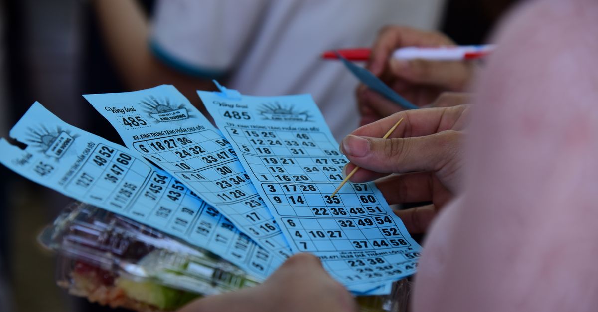 People playing bingo indoors, holding blue bingo cards with pen and markers.