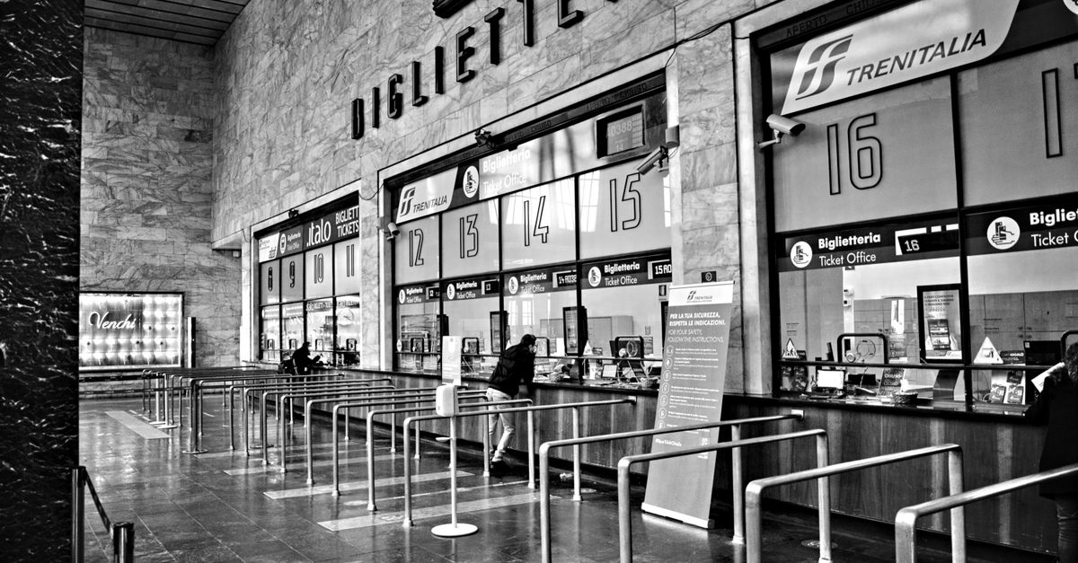 Monochrome view of an indoor train ticket area with counters and queue barriers.