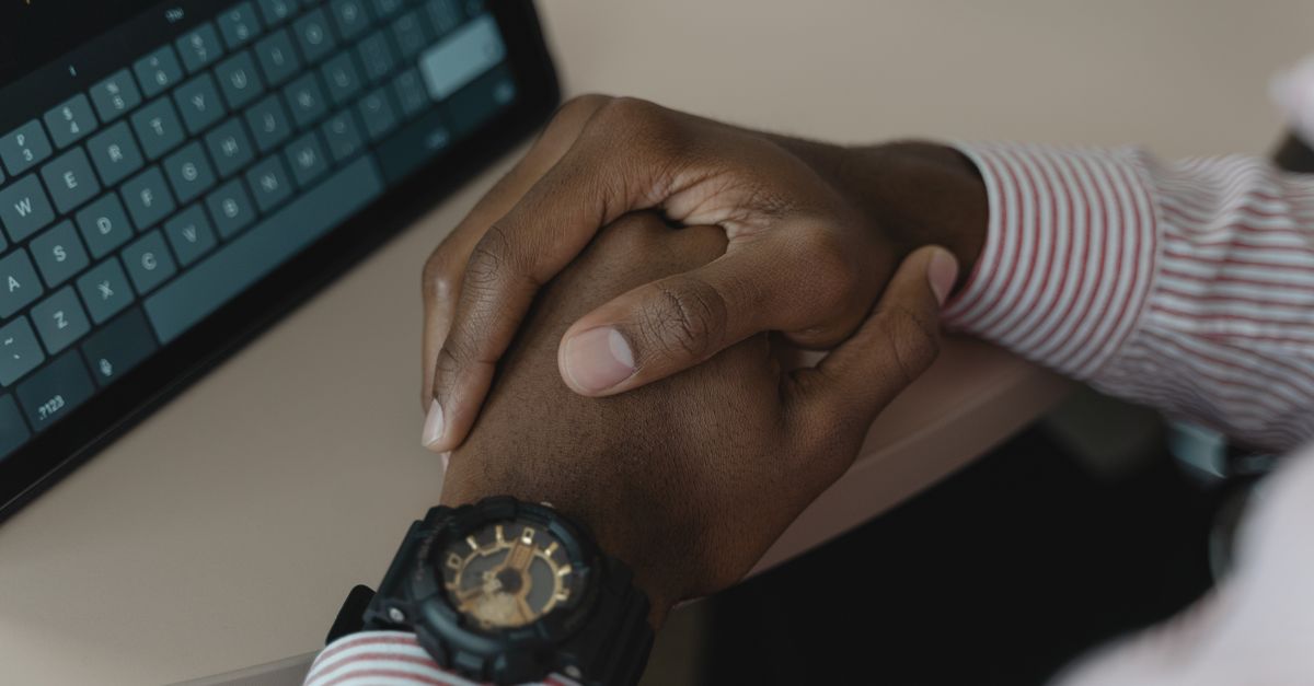 Close-up image of crossed hands wearing a watch near a tablet keyboard.