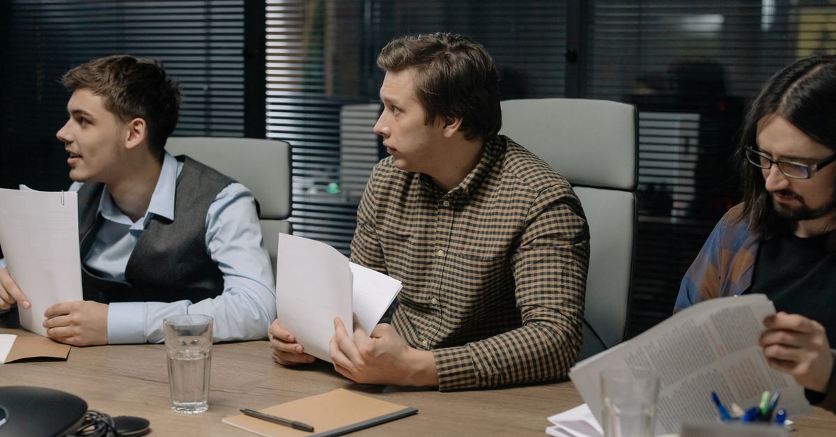 Three male colleagues engage in a business meeting discussing documents around a table.