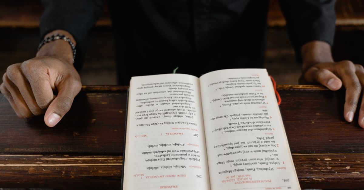 A close-up view of a priest reading an open bible during a church service, focus on hands and book.