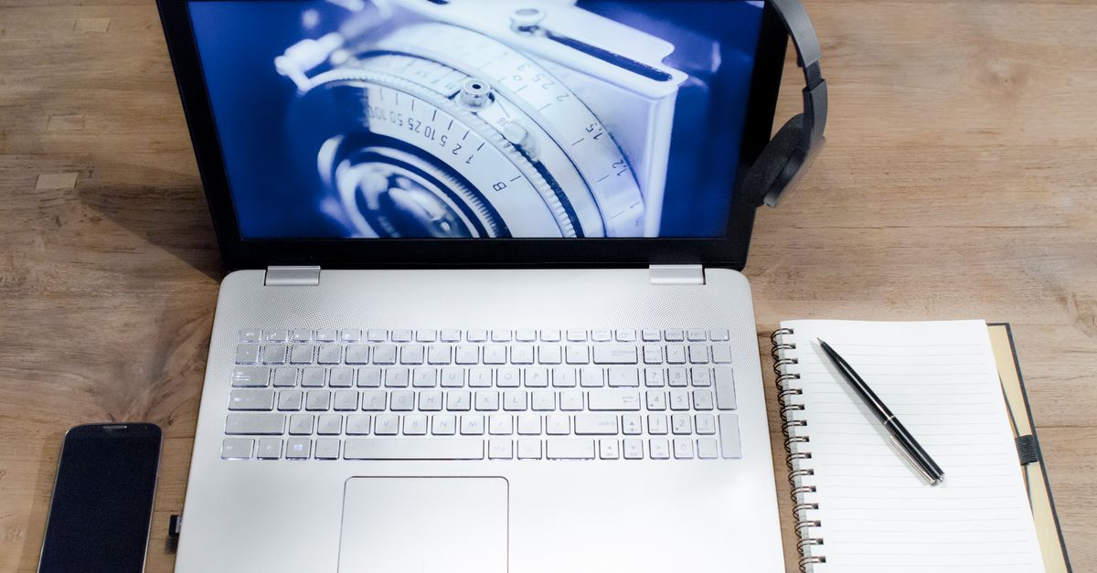Top view of a modern workspace with a laptop, smartphone, headphones, and a notebook on a wooden desk.
