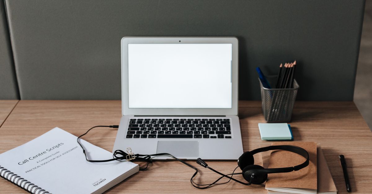 Minimalist workspace with laptop, headset, and call center scripts on a wooden desk.