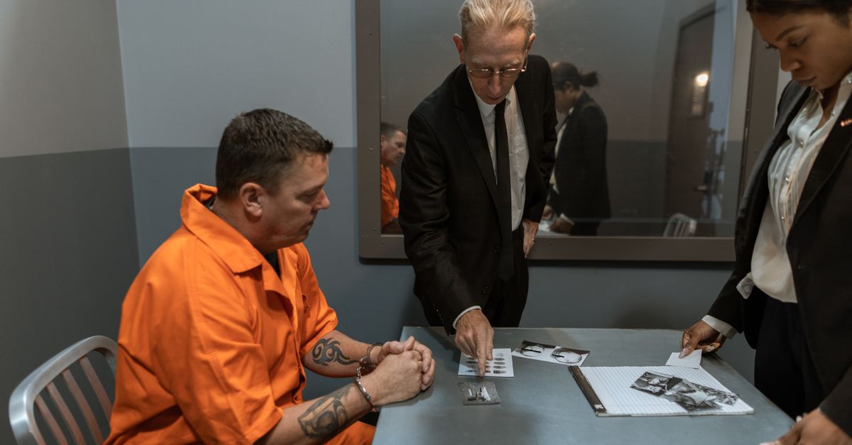 A tense interrogation scene featuring a prisoner in an orange jumpsuit with detectives in a dimly lit room.