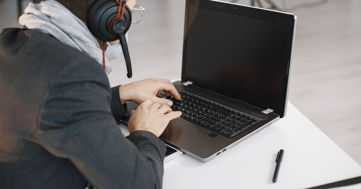 Focused man wearing headphones using a laptop for remote work in a modern office setting.