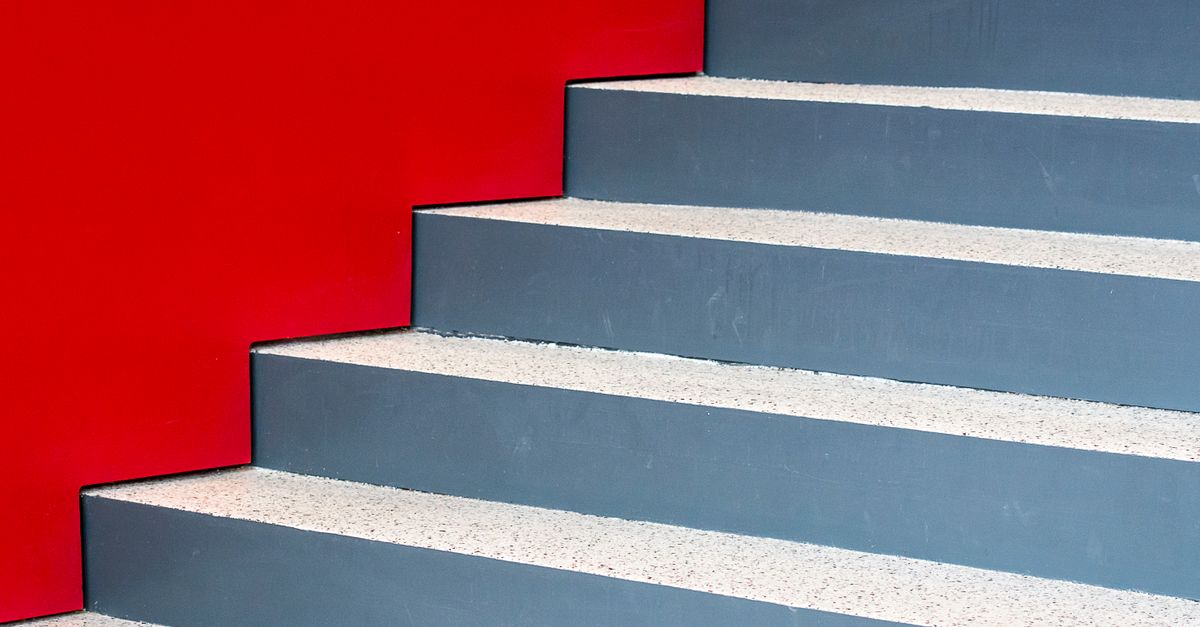 Image of a modern staircase against a vibrant red wall, highlighting geometric design and contrast.