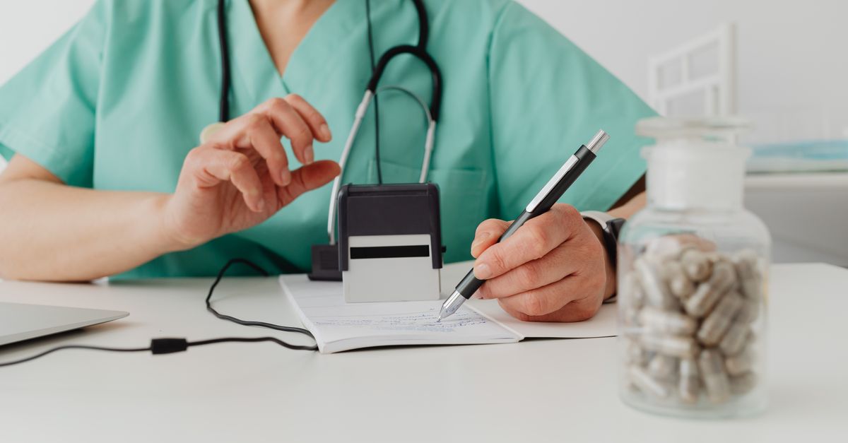 A medical professional writing a prescription in a clinical setting.
