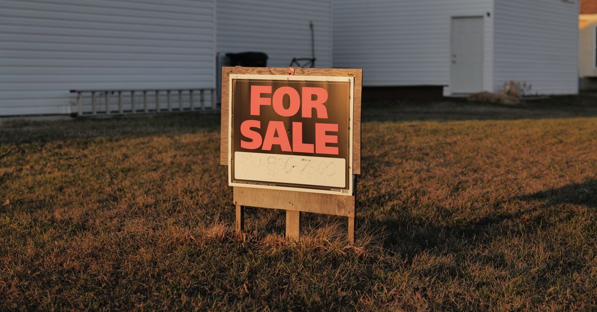 Close-up of a 'For Sale' sign in a suburban yard, indicating a property for sale.
