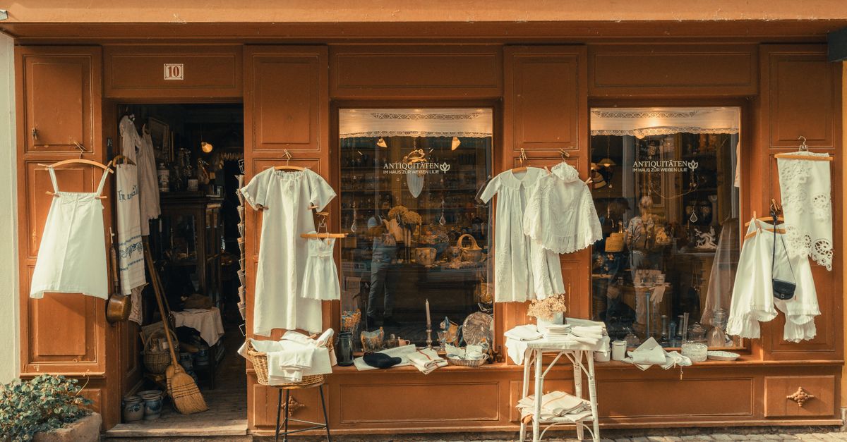 A picturesque antique shopfront displaying vintage linens and decor in warm, muted tones.
