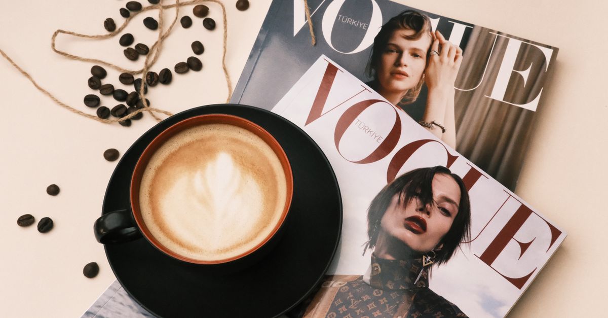 A cozy cafe table with a latte and Vogue magazines, perfect for stylish relaxation.