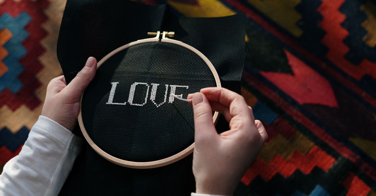Hands embroidering 'LOVE' on black fabric using a wooden hoop, close-up view.
