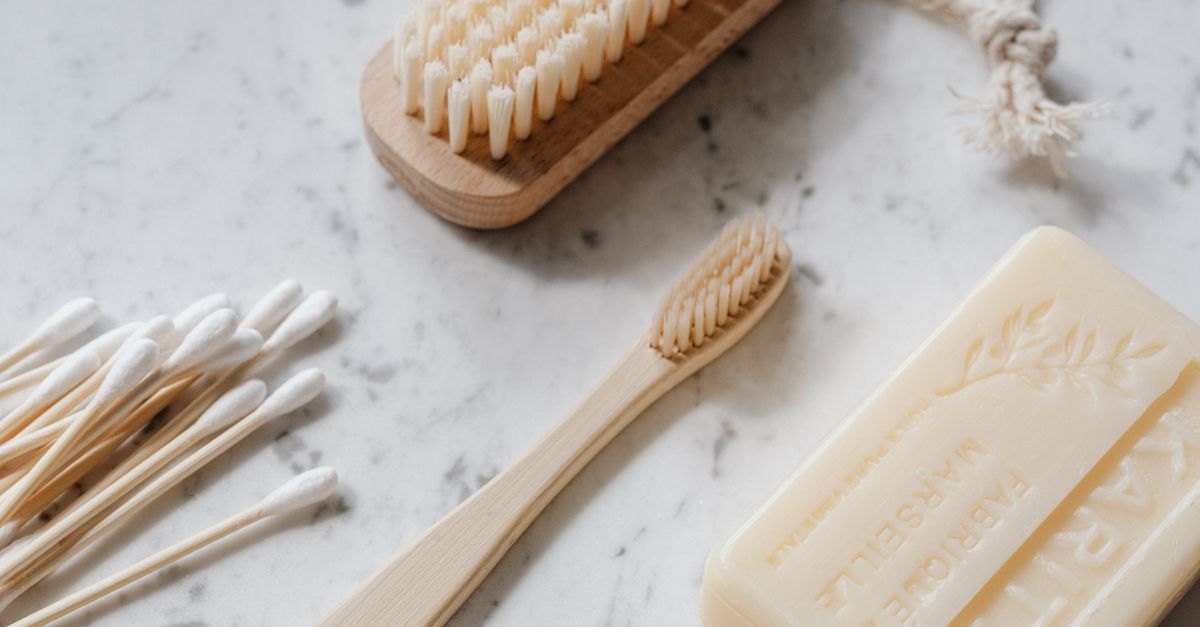 From above closeup of wooden cleaning brush and toothbrush and cotton swabs and soap placed on marble surface