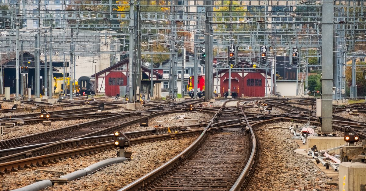 View of multiple railway tracks with signals and buildings in an urban setting during daytime.