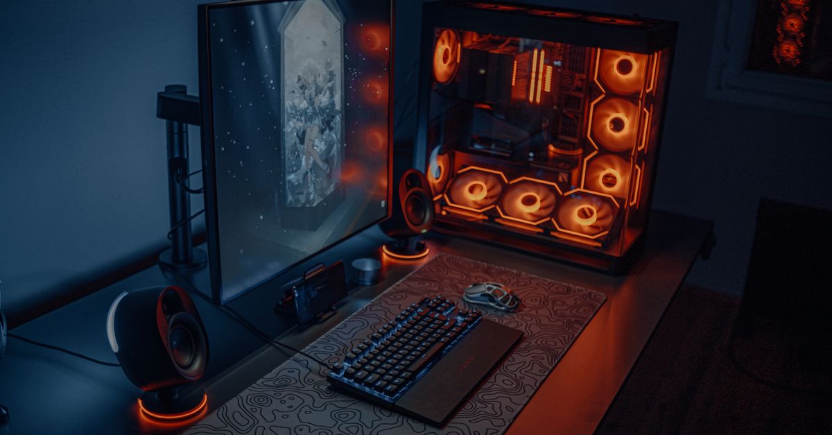 Sleek gaming desk setup featuring RGB lighting, large monitor, and gaming PC with glowing fans.