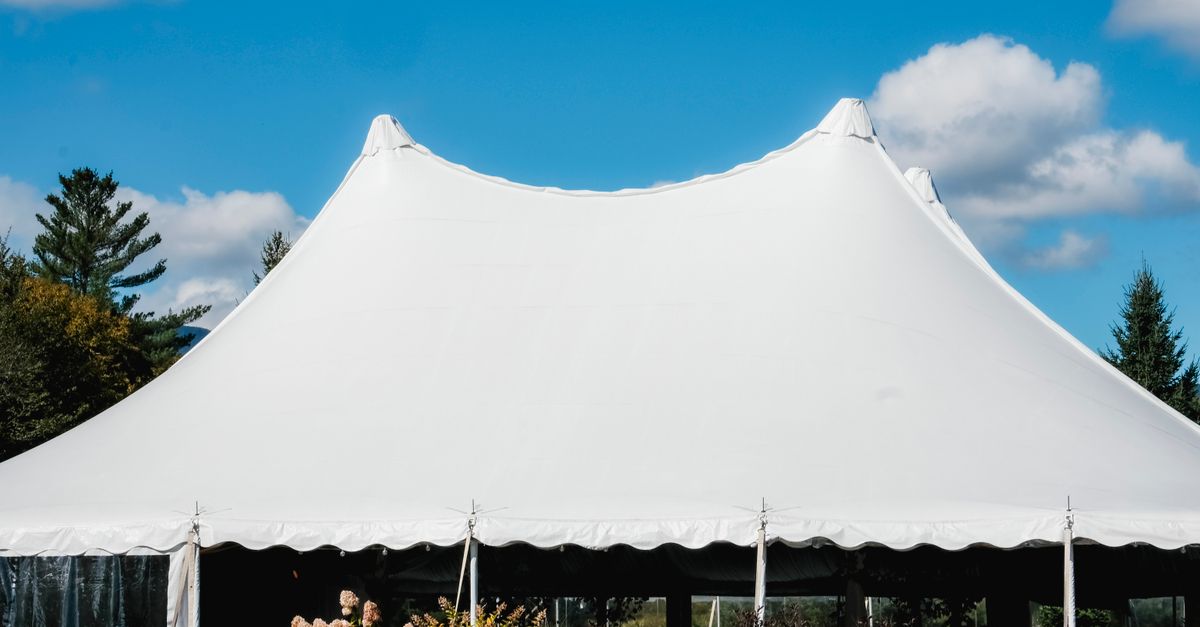 A sleek white tent set up outdoors under a vibrant blue sky with fluffy clouds.