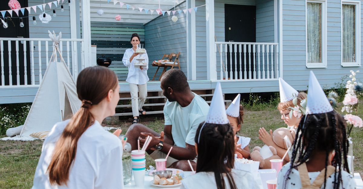 Children and adults celebrating a birthday outdoors with food and decorations.