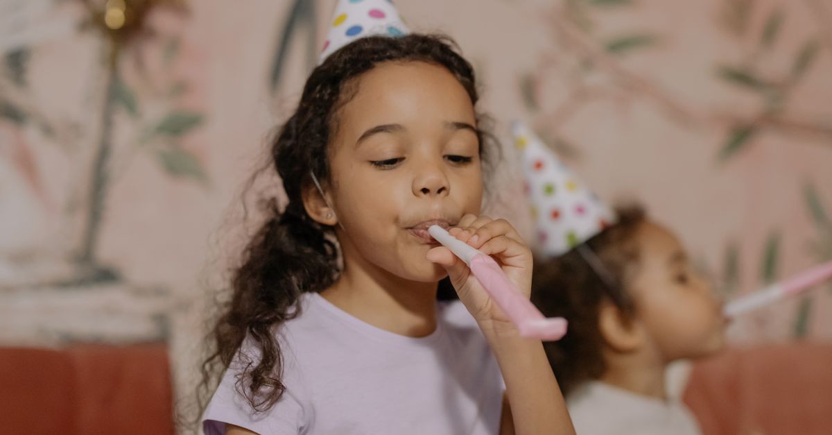 Two young girls in party hats enjoying a birthday party indoors.