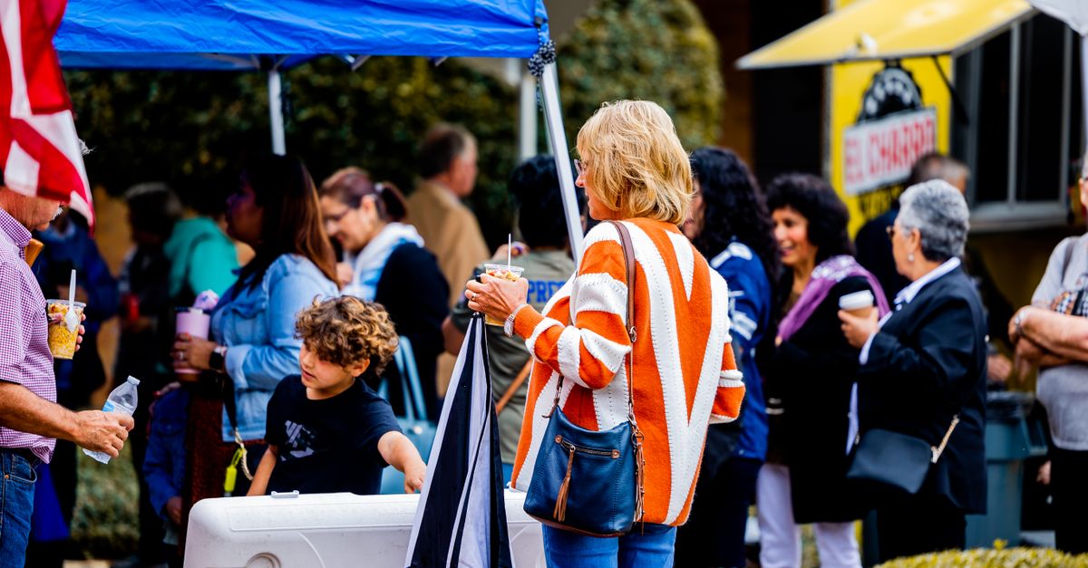 People enjoying a lively outdoor market scene with food and drinks in hand. Perfect for lifestyle and community themes.