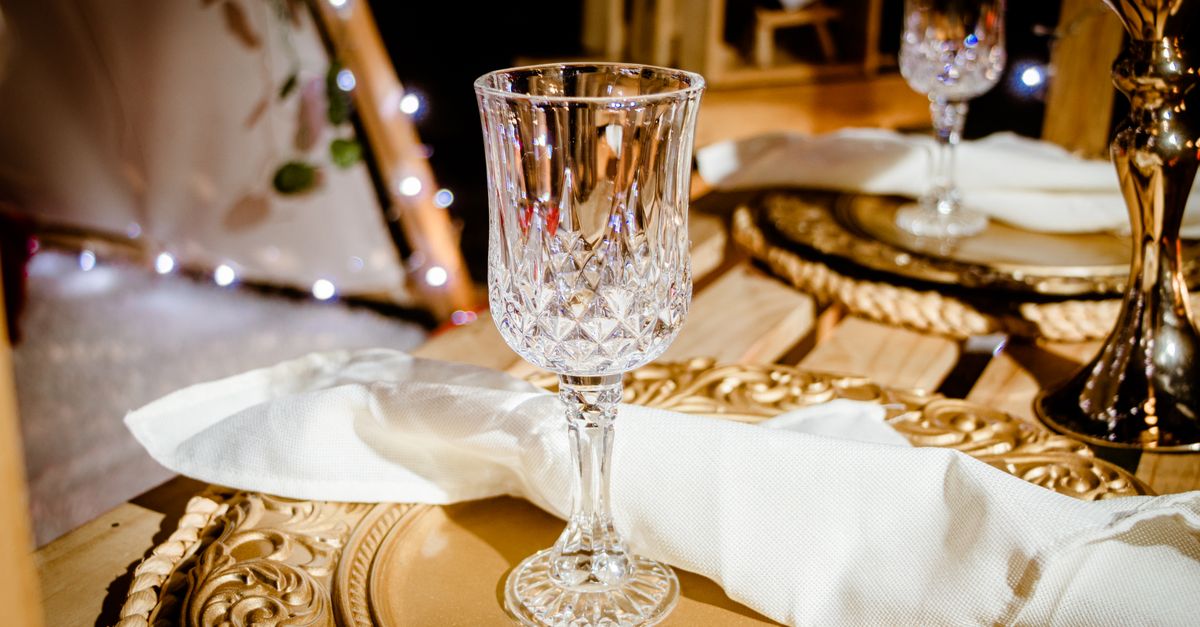 Luxurious dining setup with crystal glass on ornate gold plate and napkin.