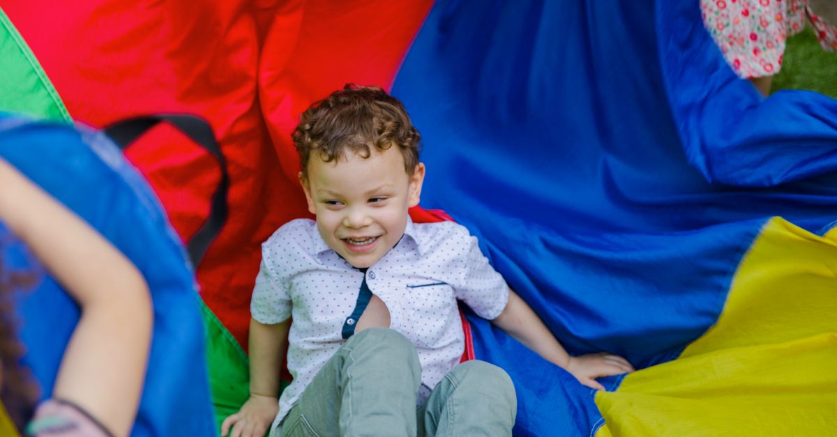 A child having fun with colorful fabric at an outdoor party. Vibrant and playful.