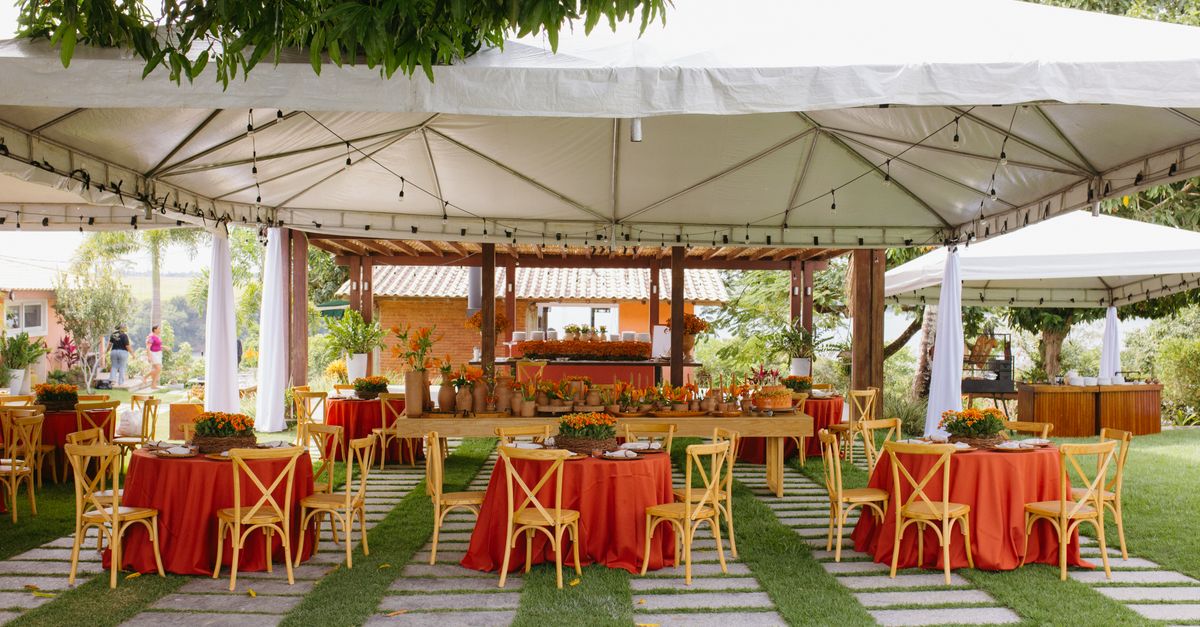 Beautifully arranged outdoor wedding setup with red and orange decor under a white canopy.