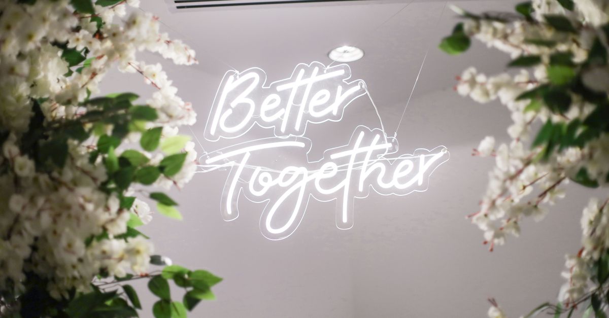 Elegant floral arrangements framing a glowing 'Better Together' neon sign at an indoor event.