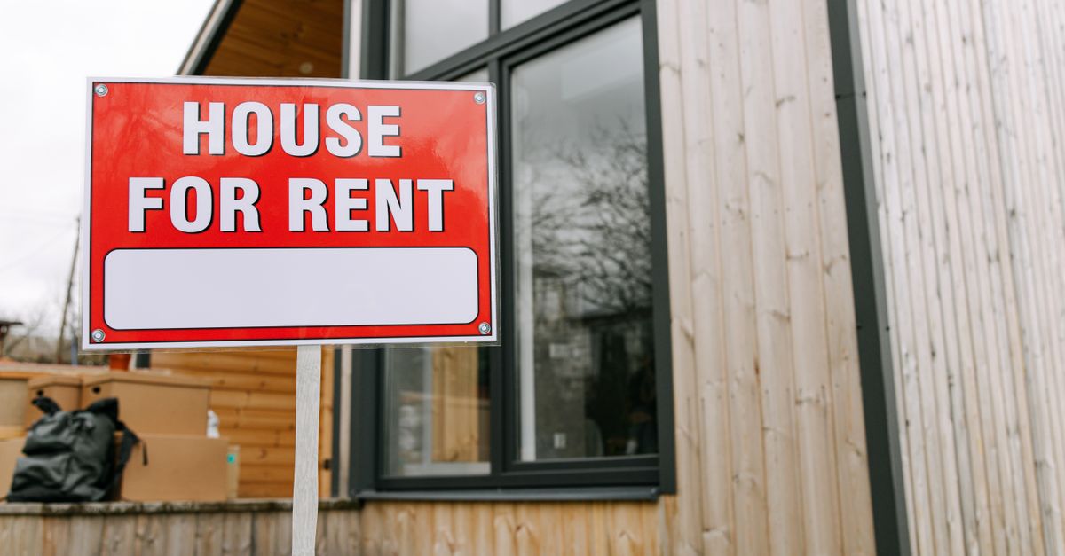 Red 'House for Rent' sign outside modern wooden house.