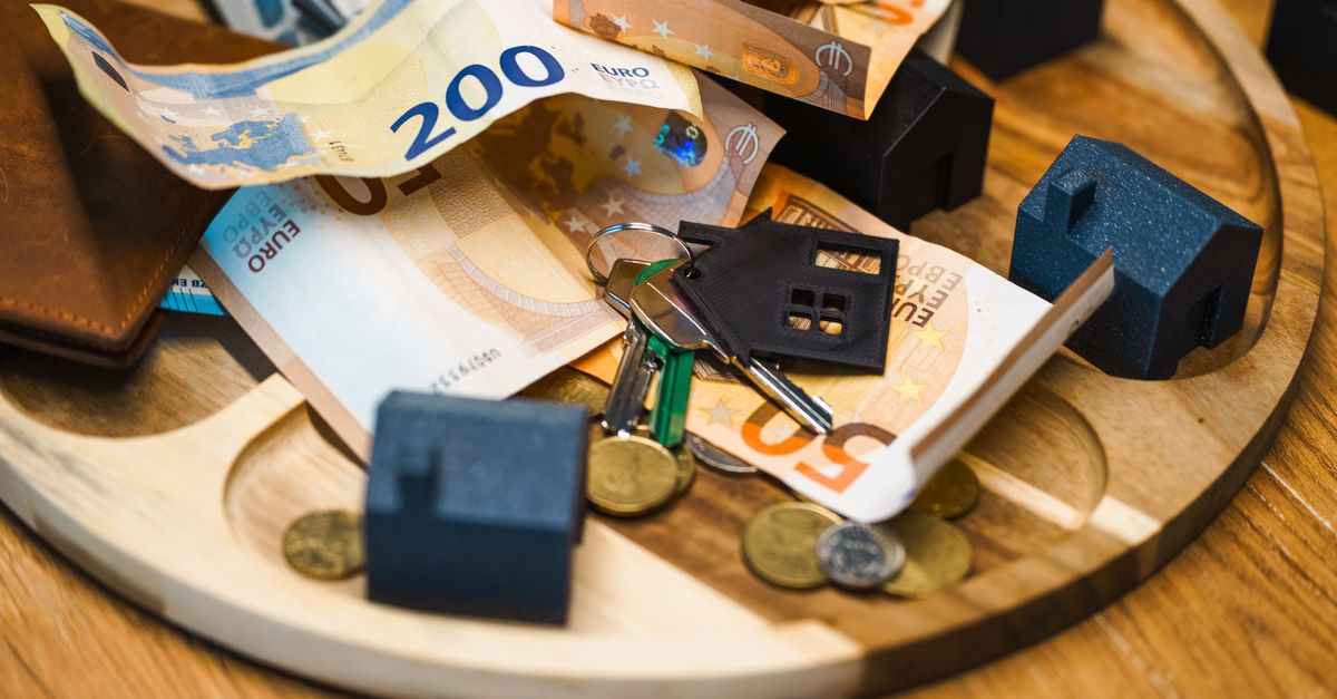 Euro currency, keys, and miniature houses symbolize real estate and finance concepts.